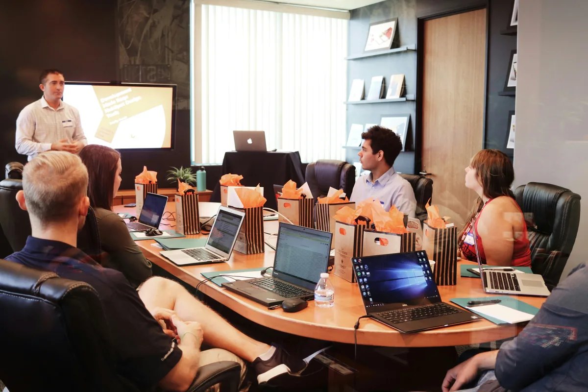 A trainer presenting to a group in a conference room, participants with laptops open